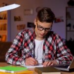 A boy in red shirt sitting on chair and writing essay