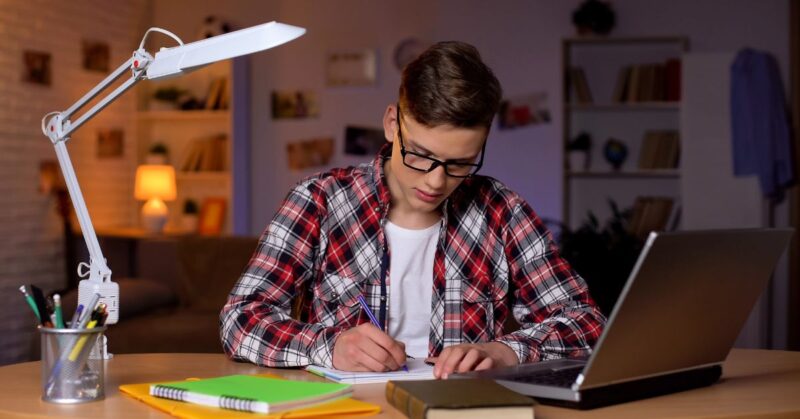 A boy in red shirt sitting on chair and writing essay