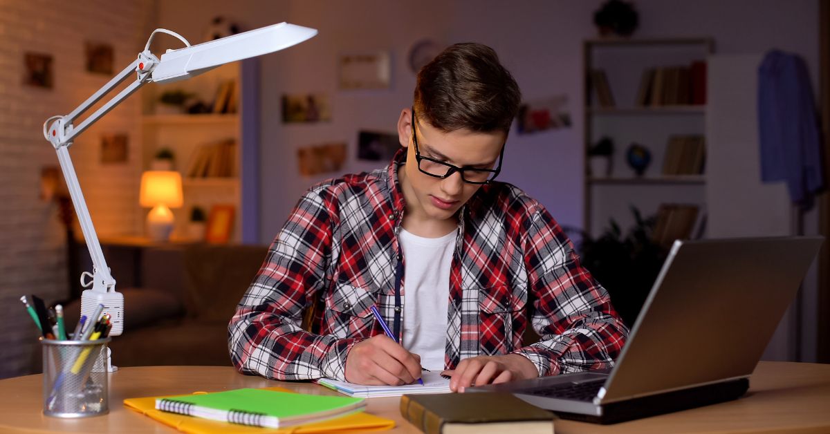 A boy in red shirt sitting on chair and writing essay