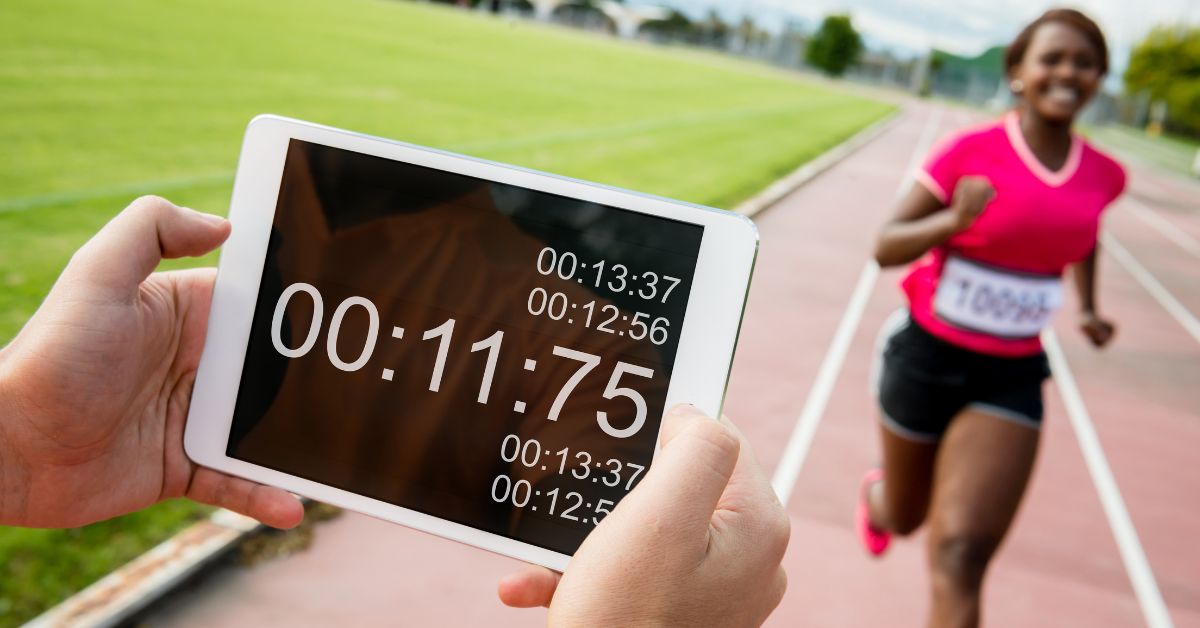 a girl runing on track while coach recording time on a device