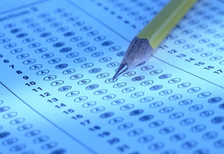A close-up of a sharpened yellow pencil resting on a standardized multiple-choice answer sheet, with several answer bubbles filled in.