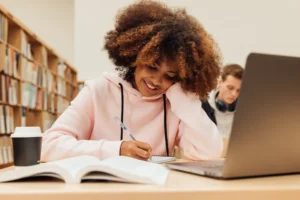 smiling-student-with-curly-hair-writing-on-notebook