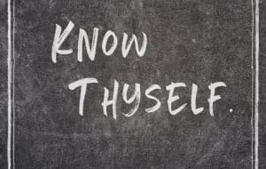 The phrase Know Thyself. is written in bold, white, handwritten-style letters on a dark chalkboard background with thin vertical white lines framing the sides.