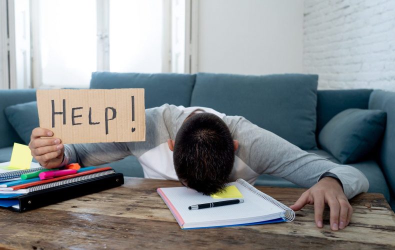 Young tired and stressed student working on his homework, masters feeling desperate and frustrated asking for help. In over Education, learning difficulties, finals exams and emotional stress concept.