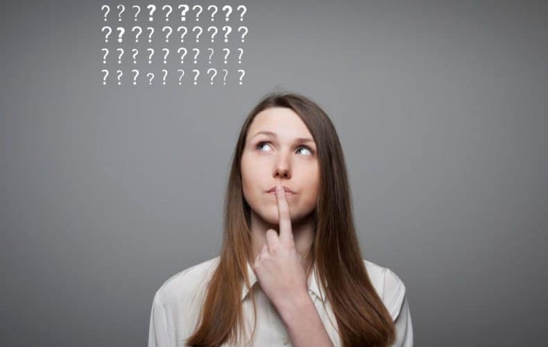 A woman with long brown hair looks up thoughtfully with her finger on her lips. Above her head are rows of question marks on a gray background, suggesting she is thinking or unsure.