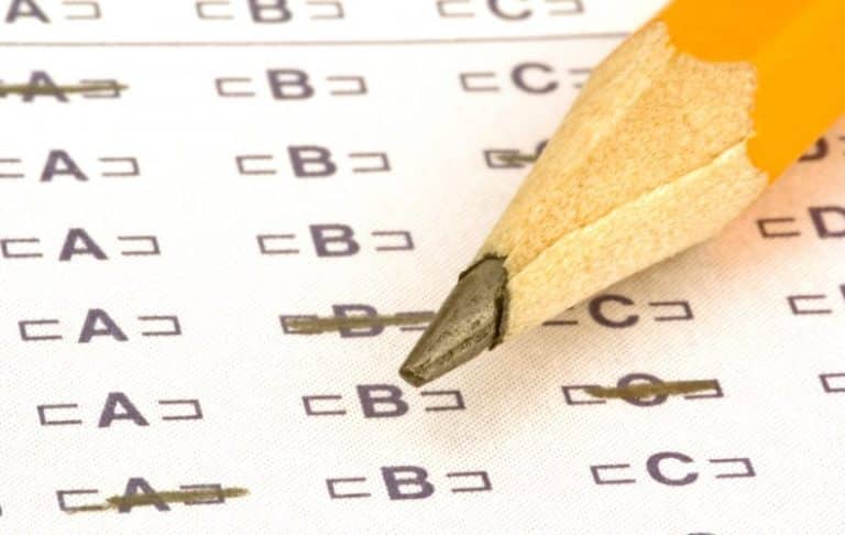 A close-up of a sharpened yellow pencil resting on a multiple-choice test answer sheet, with several answers filled in and one answer being marked.