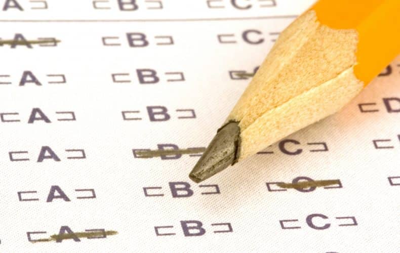 A close-up of a sharpened yellow pencil resting on a multiple-choice test answer sheet, with several answers filled in and one answer being marked.